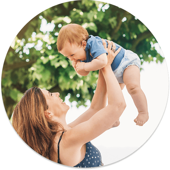 A mother lifts her baby into the air, smiling